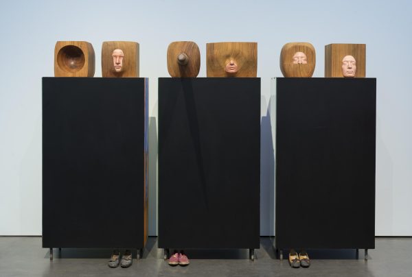 Three black boxes each with two heads carved out of brown cubes in various ways. Shoes lay at the bottom of a few of the boxes.
