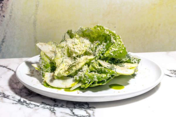 A green salad with dill, apples, and grated cheese on a white plate