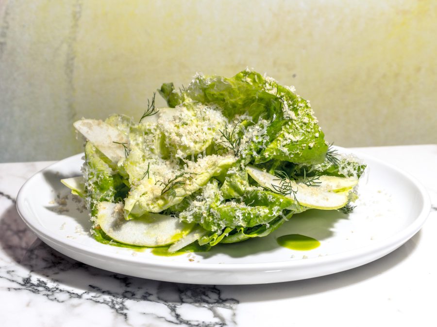 A green salad with dill, apples, and grated cheese on a white plate