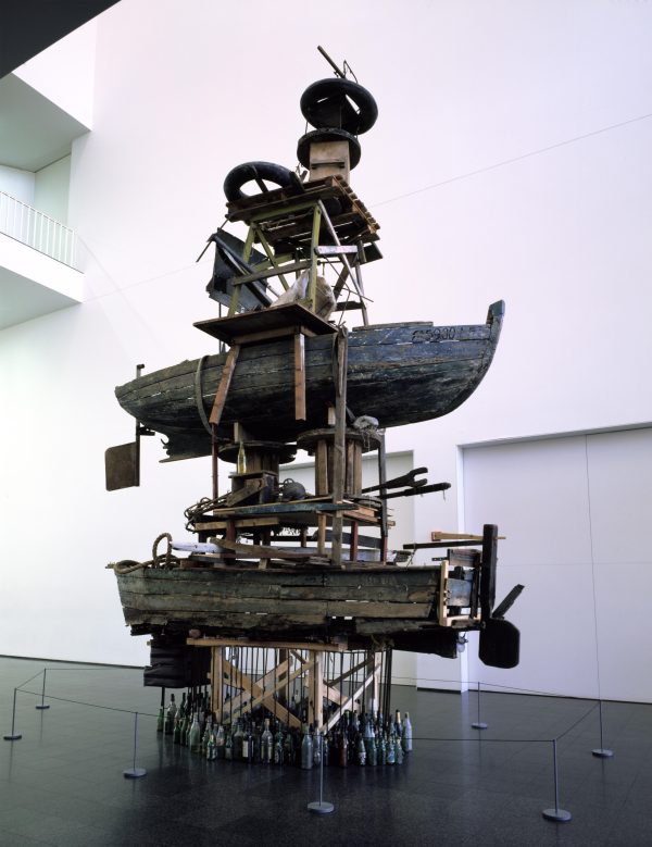 A sculpture of boats and other wooden objects piled on top of each other in a white open space