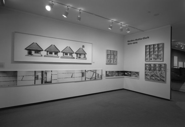 Black and white photo of a gallery installation with artworks spanning two walls