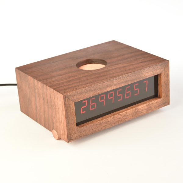 A rectangular wooden digital clock displaying the number 26,995,657