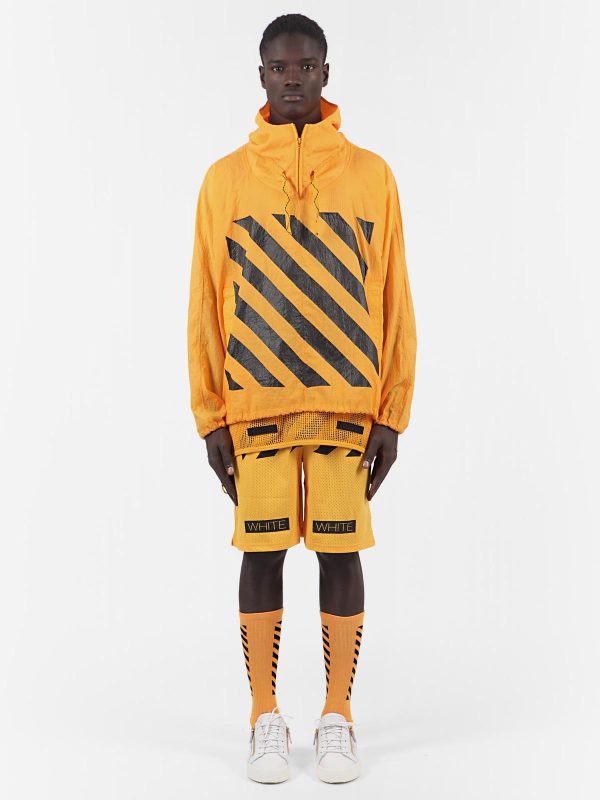 A dark-skinned model stands rigidly while wearing a rich yellow outfit of a striped hoodie, long shorts, and high striped socks with white sneakers.