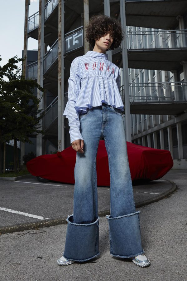 A model poses in an urban landscape while wearing a frilly shirt with the word 