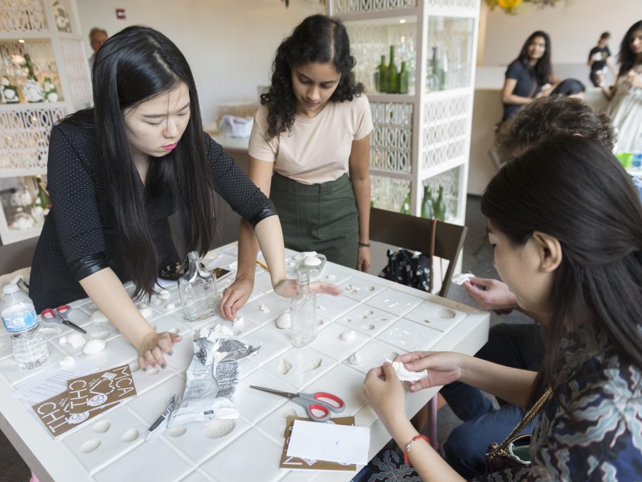 Four people craft seashells by pressing clay into molds on a table.