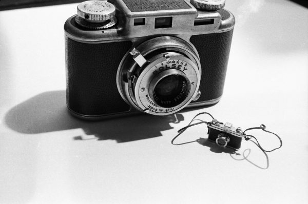 A black-and-white photo shows a film camera next to a much smaller version of itself.