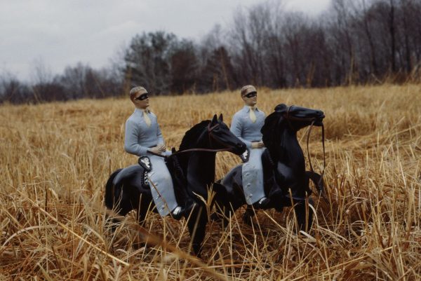 Two cowboy figurines and their horses stand in a field of dry grass.