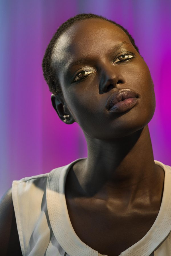 A dark-skinned person in front of a luminous violet background gazes upward past you, but upon closer inspection it seems their eyes are not real.