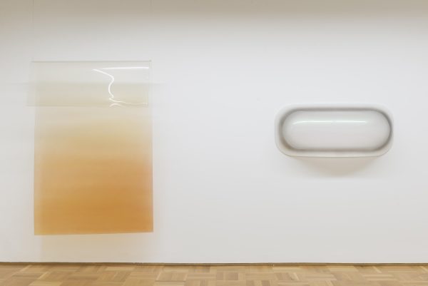 Two shiny, plastic-like minimal sculptures are mounted on a white wall.