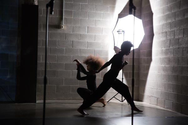 Two dancers silhouetted in pose set against a concrete wall