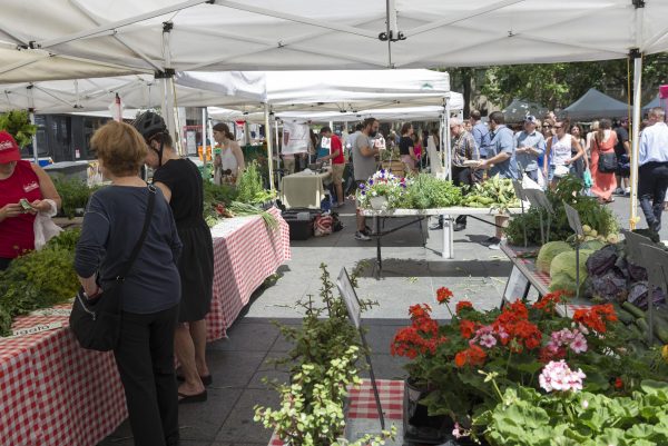 A bustling outdoor plaza filled with tents and tables where people are buying vegetables and plants.