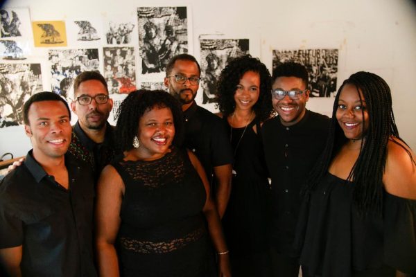 A group of people all dressed in black posing in front of a wall of images