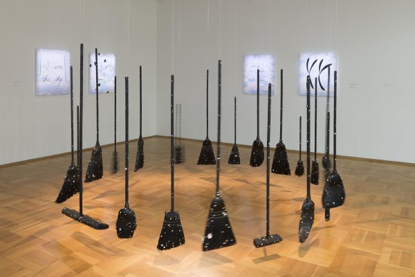 Various types of brooms hang in a circle in a gallery space