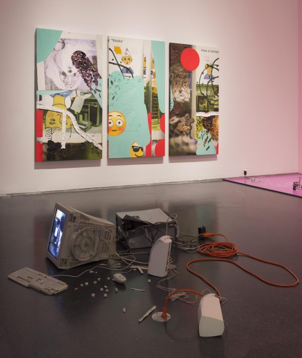 Pieces of an old desktop computer are strewn about the floor of a gallery with other artworks hanging on the walls nearby