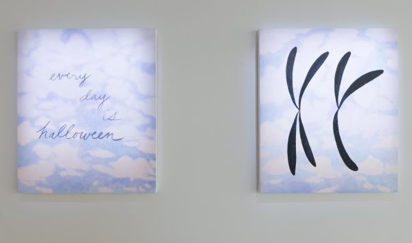 Two paintings of idyllic cloudy blue skies hang side by side. One reads 