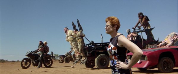 Pauline Hanson is inserted into a scene from Mad Max: Fury Road. She stands stoically, facing out to our left.