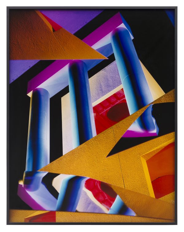 Collage of colorful geometric objects including blue and purple columns and yellow triangles layered on top of each other against a black background