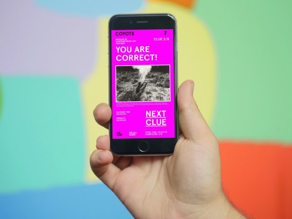 A light-skinned hand holds up a smartphone with the screen facing you. The screen reads, 