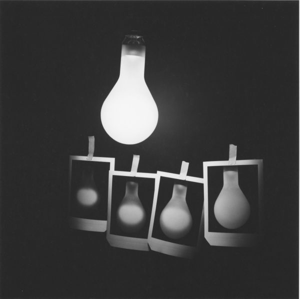 A single lightbulb just barely illuminates four images held up by clothes pins of single lightbulbs