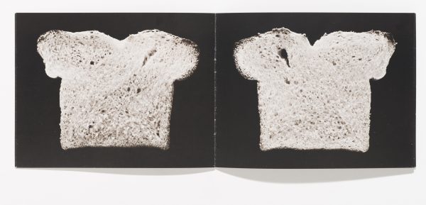 An open book featuring a slice of bread against a black background on each page. The slice on the right has a small air pocket in its upper left corner.