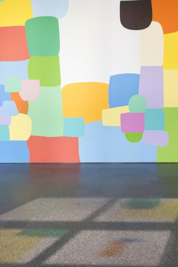 A large wall features a prominent, colorful mural. Light shining from windows casts colorful shadows on the floor.