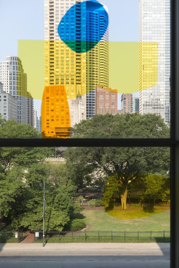A window looking out on a park and the Chicago skyline has four brightly colored splotches of yellow, orange, and blue.