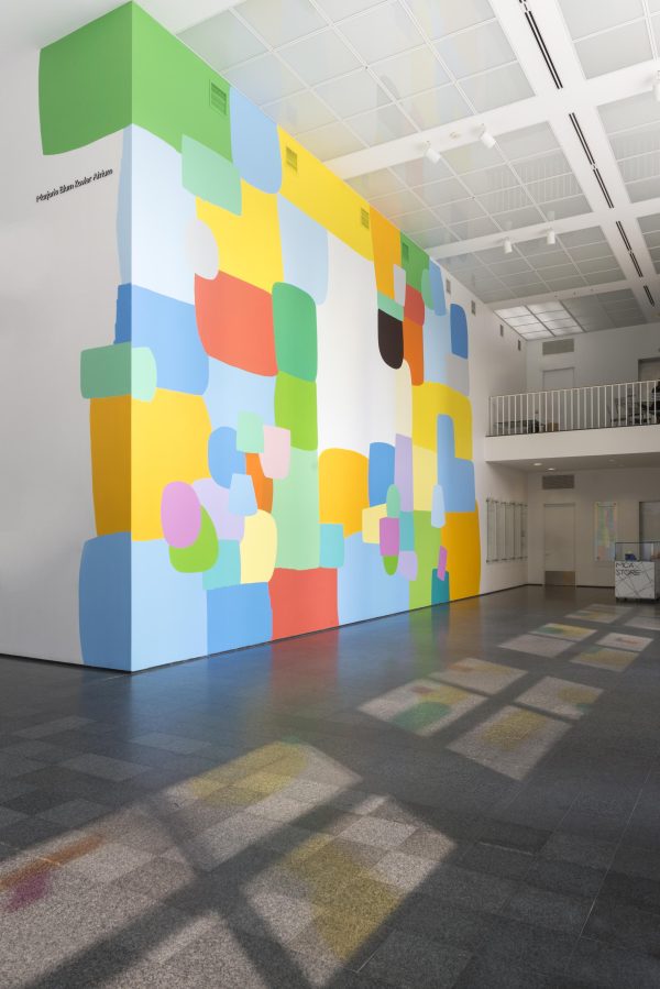 The MCA Atrium features a prominent, colorful mural on the walls and spots of illuminated color on the floor.
