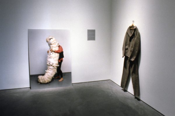 A gallery view of two works of art; one a large photo and other a suit on a hanger.