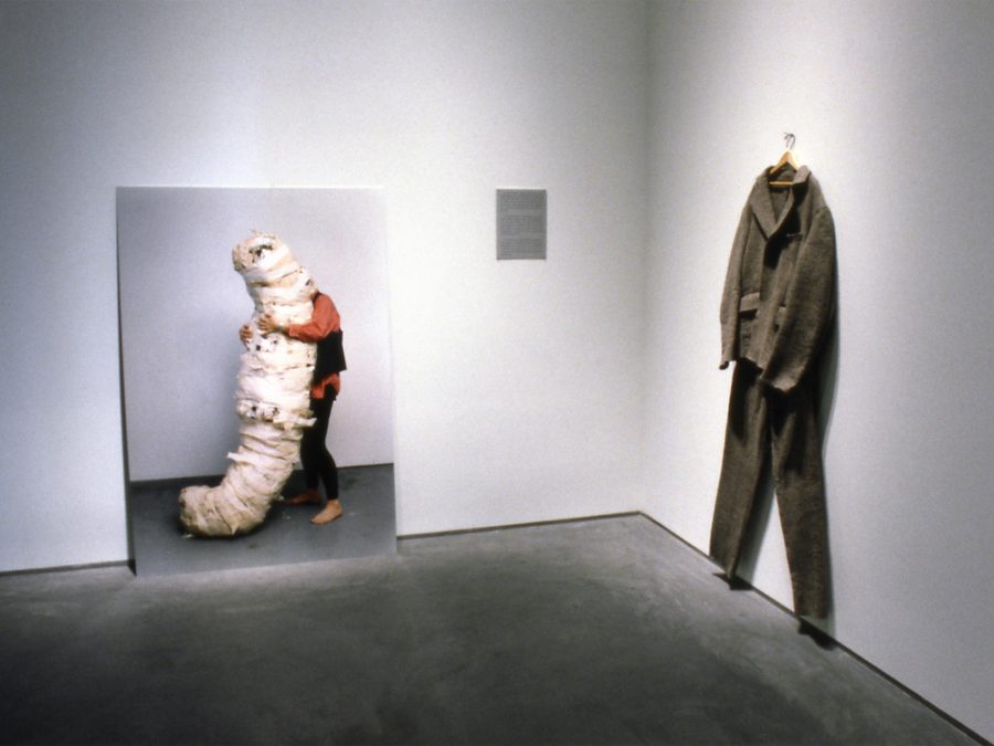A gallery view of two works of art; one a large photo and other a suit on a hanger.