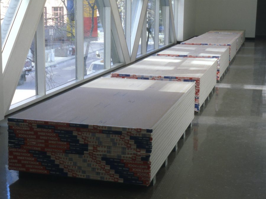Gallery view of four equal stacks of drywall in front of a window.