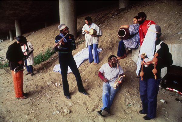 A group of people gather in the sand under an underpass