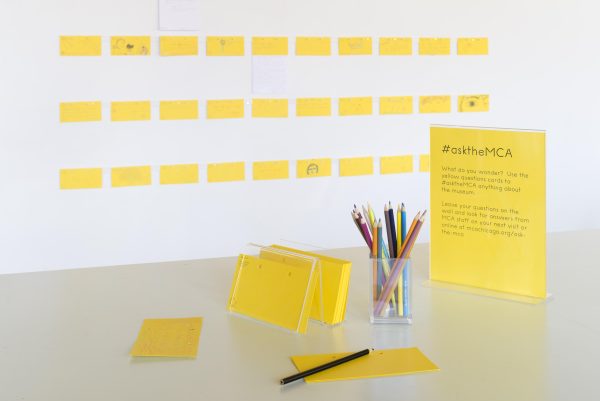 A table with pens and note cards next to a placard with instructions titled Ask the MCA
