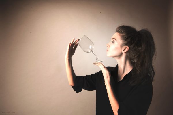 A woman in a black long-sleeved shirt with the sleeves rolled up examines a wine glass against a beige backdrop