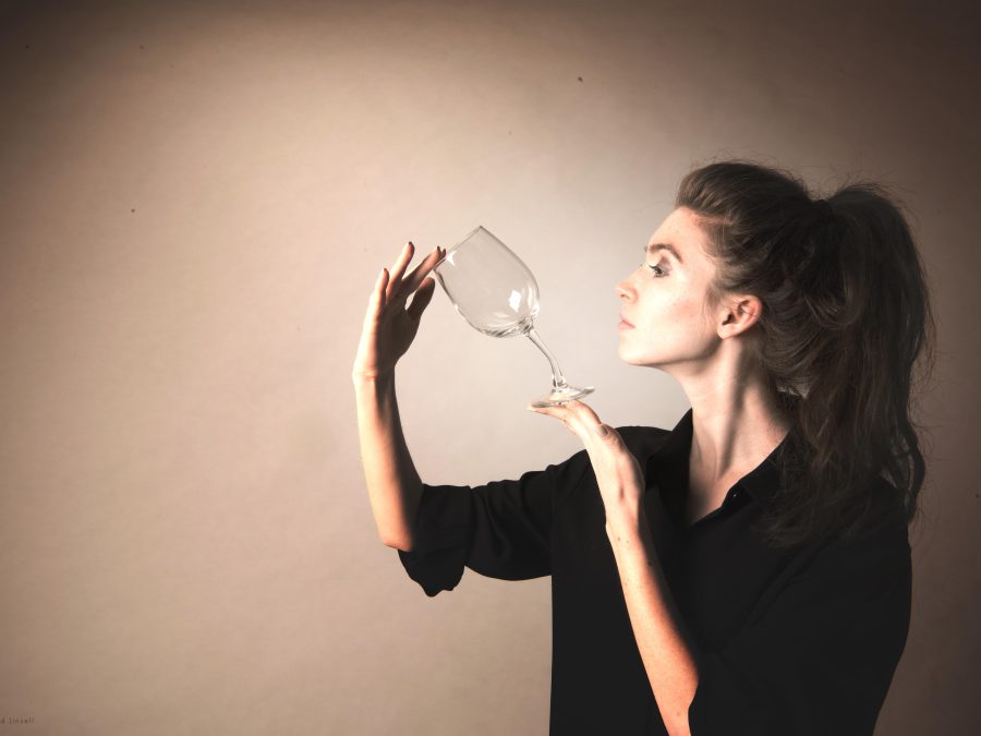 A woman in a black long-sleeved shirt with the sleeves rolled up examines a wine glass against a beige backdrop