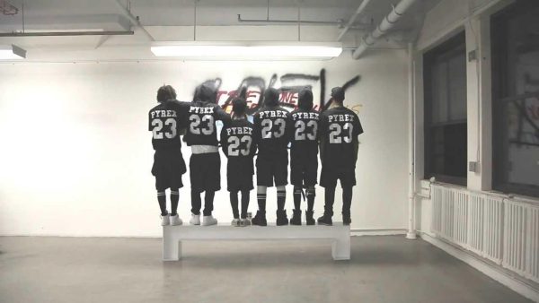 The backs of six people standing on a bench in a gallery all wearing black number 23 jerseys