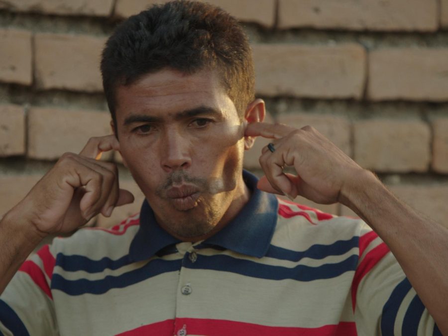 A man wearing a striped polo shirt purses his lips while placing his index fingers in each ear.