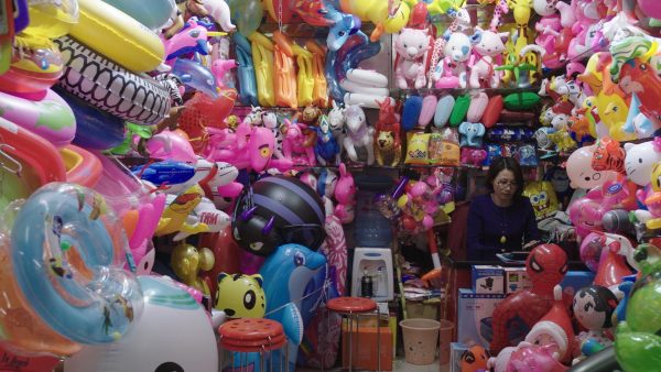 A woman sits in a room with walls fully covered with colorful inflatable animals and cartoon characters.
