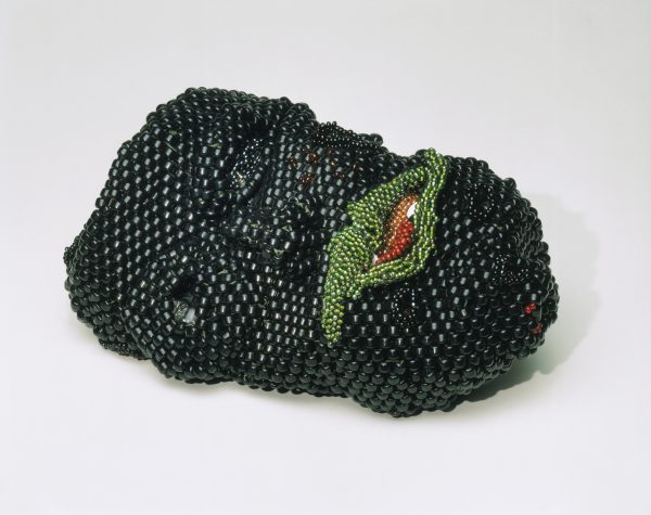 Sculpture of a person's face made mostly of black beeds, with green beads for the mouth