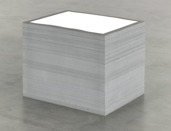 A tall stack of paper on a gray concrete floor. The top piece of paper is printed with a black outline around a solid white rectangle.