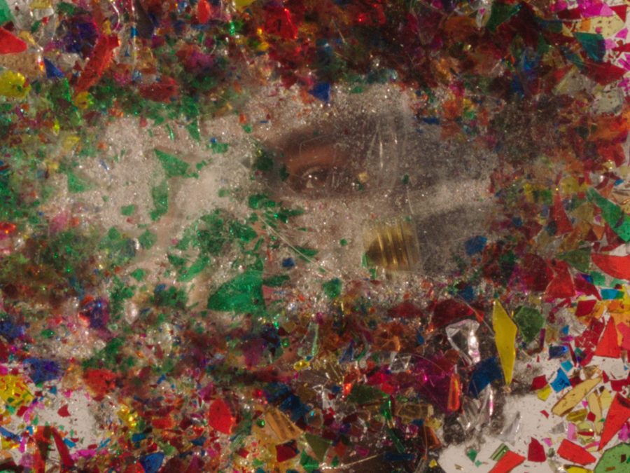 Colorful pieces of broken glass surround a clear space where a person's eye is just slightly visible
