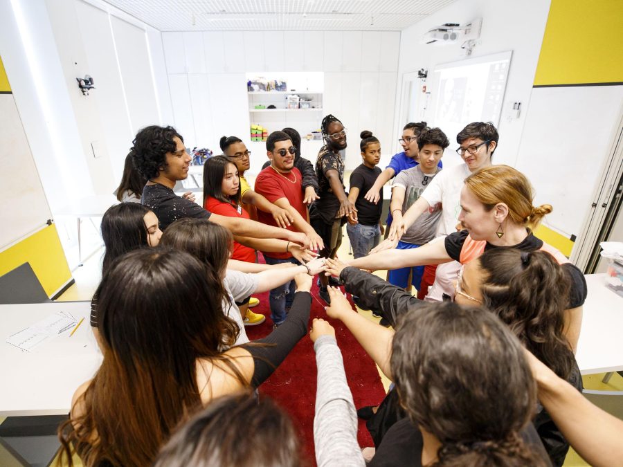 A group of people stand in a circle with all hands in