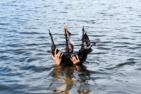 Two hands hold an intricate toy wooden ship out of the water