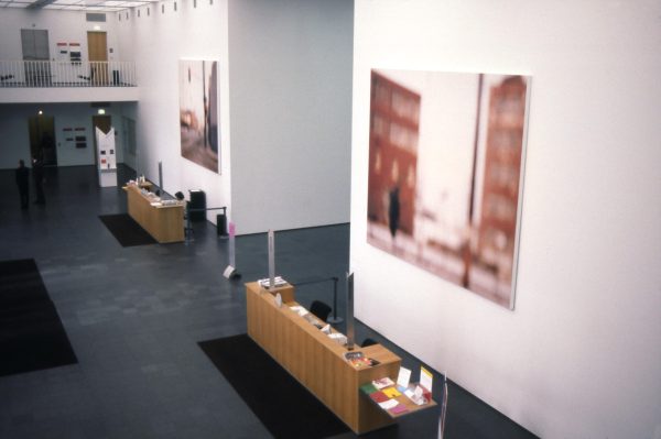 Two large, blurry images of streets hang above two sets of desks in a two-story space with a balcony overlooking it to the far left side