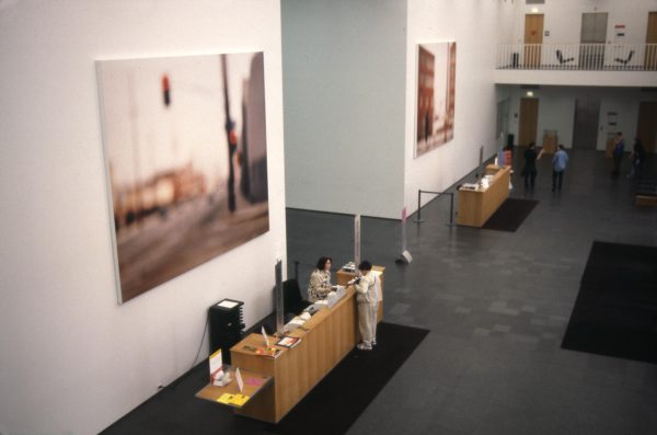 Two large, blurry images of streets hang above two sets of desks in a two-story space with a balcony overlooking it to the far right side
