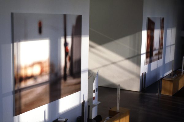 Two large, blurry images of streets hang in a two-story space lit dramatically by long shadows cast by sunlight