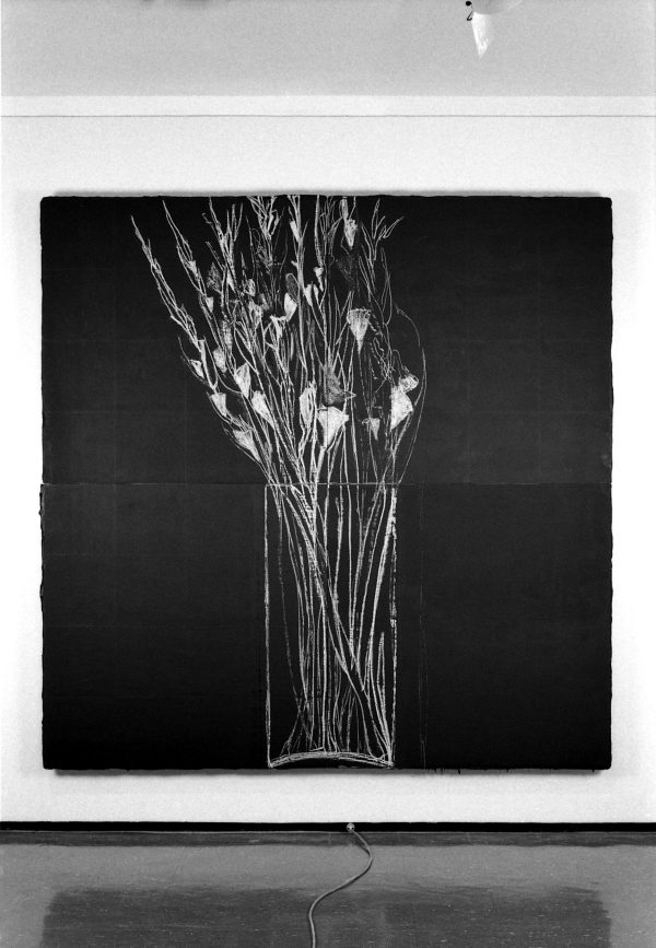 Large square black artwork on a white wall with thin white lines gathered in the middle, resembling an x-ray of a bouquet of dead flowers.