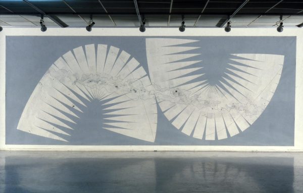 A rectangular large work with a light blue-gray background and a series of white triangles that have been placed together so closely that they make up two shapes that look like a lowercase n and a U.