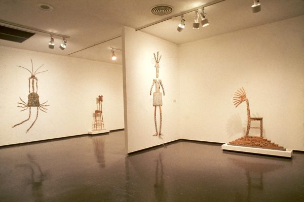 Wooden sculptures hung on the walls and placed on pedestals in a two gallery spaces cast in a yellow light