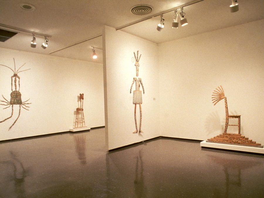 Wooden sculptures hung on the walls and placed on pedestals in a two gallery spaces cast in a yellow light