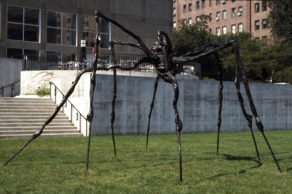 A larger black sculpture resembling a giant spider in the middle of a park with steps and a concrete wall behind it